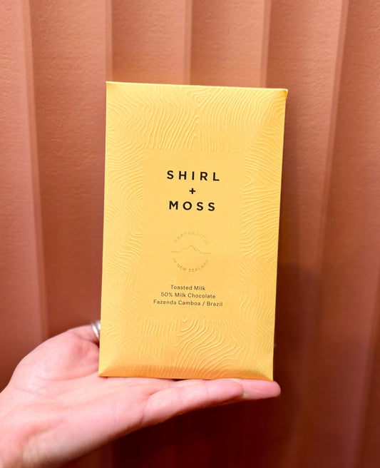 Hand holding a Shirl + Moss chocolate bar in yellow packaging