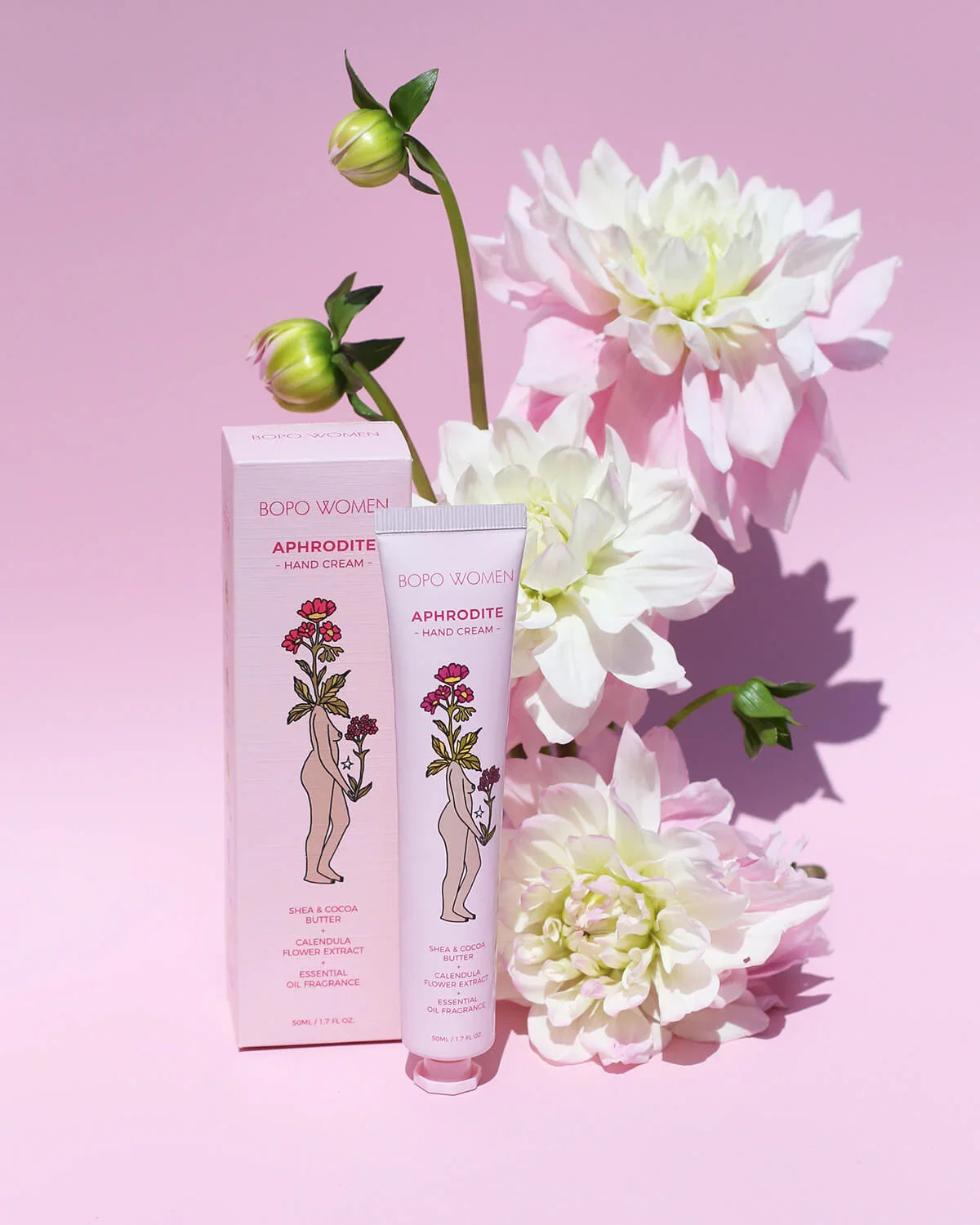 Aphrodite luxury hand cream and box styled with dahlias on a pink background