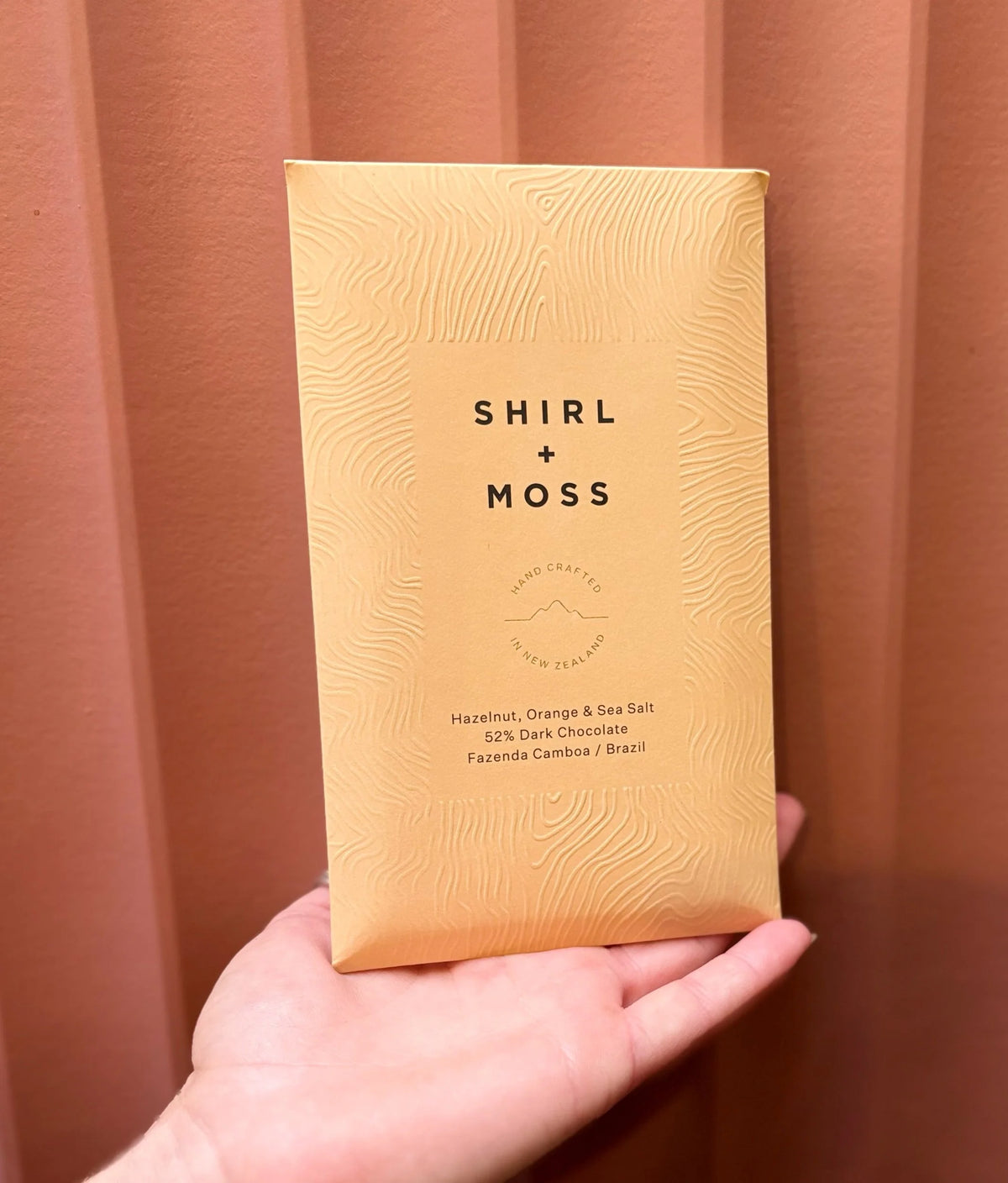 Hand holding a Shirl + Moss chocolate bar in peach packaging