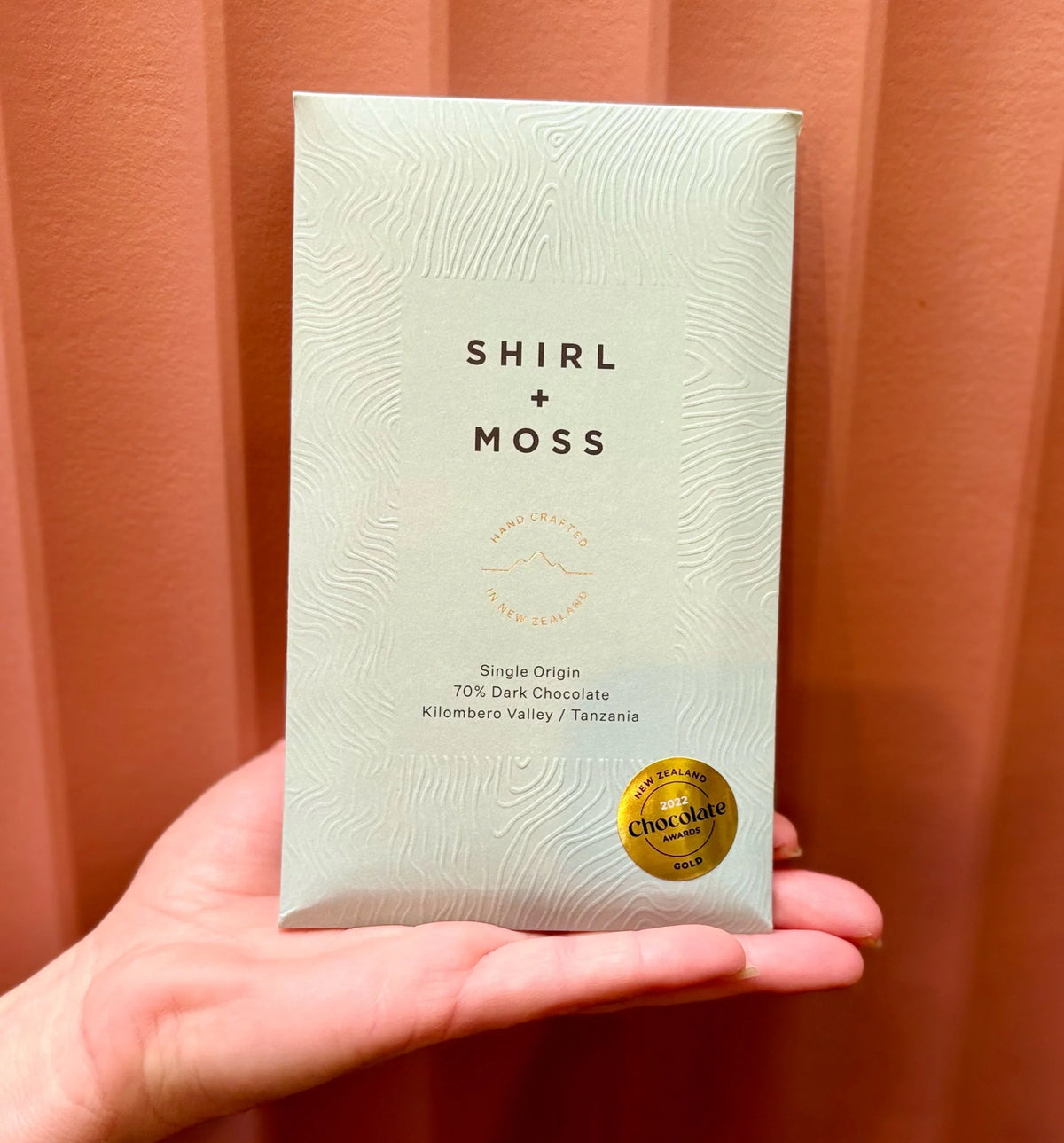 Hand holding a Shirl + Moss chocolate bar in green packaging