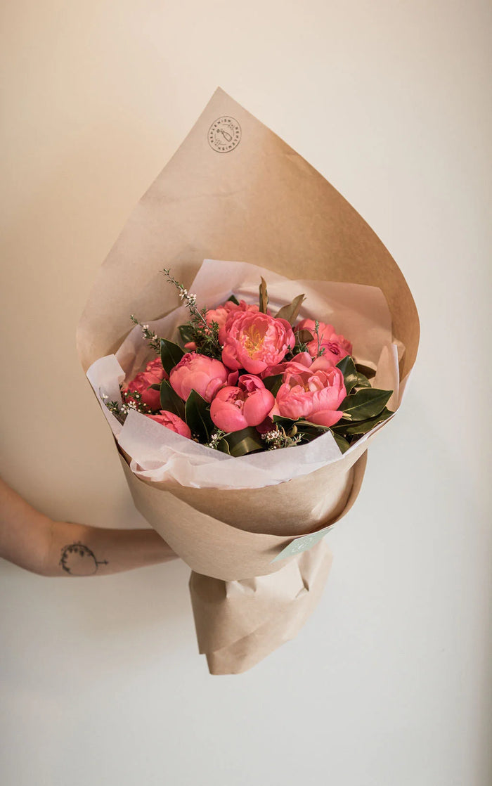Hand-tied bouquet of coral pink peonies in kraft paper