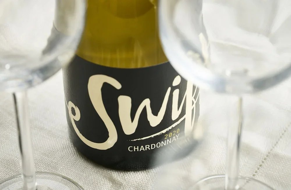 Close-up of the Swift Wines Chardonnay label with wine glasses