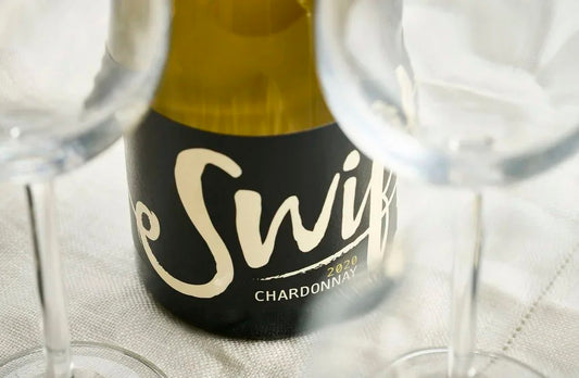 Close-up of the Swift Wines Chardonnay label with wine glasses